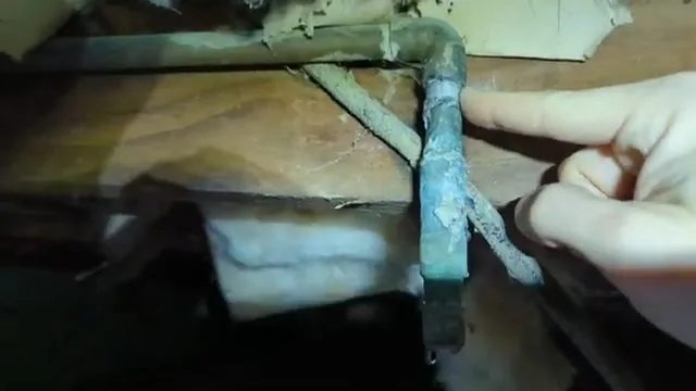 Fingertip pressing a green corroded copper elbow under a floor