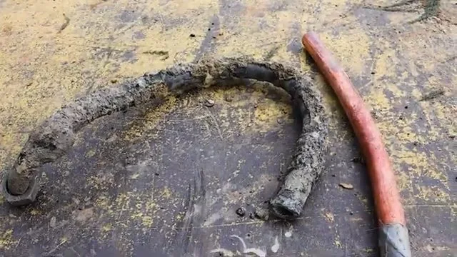 Old pipe section crusted with deposits lying beside a new copper pipe on a worn workbench