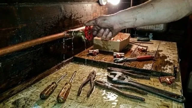 Hand on a red valve fitted to copper pipe beside loose fittings and tools on a wet table